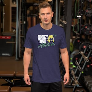 May include: A navy blue t-shirt with a distressed white graphic that says "Honky Tonk Attitude" with a yellow silhouette of a person with long hair. The graphic also includes a green signature that says "D44".