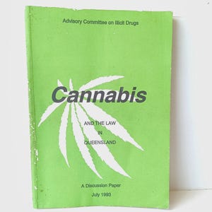 May include: A light green softcover book titled Cannabis and the Law in Queensland, A Discussion Paper, July 1993, published by the Advisory Committee on Illicit Drugs. The cover features a large white cannabis leaf graphic and dark text.