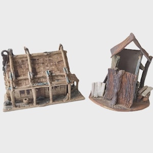 May include: Two miniature ceramic structures, resembling rustic buildings. One is a house with a thatched roof and a small porch. The other is a weathered shed with a wooden fence and bench. Both are in shades of brown and beige.