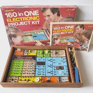 May include: A Science Fair 160 in ONE Electronic Project Kit featuring a wooden base with a colourful circuit board layout, including various electronic components, wires, and a digital display, accompanied by its original cardboard box and manual.
