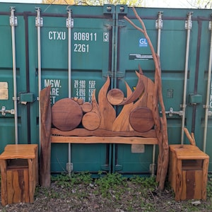May include: A handcrafted wooden bed frame with a headboard featuring circular and flame-like designs. Two matching nightstands with a rustic, natural wood finish flank the bed. The bed frame and nightstands are made of various shades of brown wood.