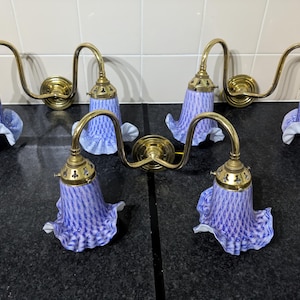May include: Six vintage wall sconces with brass fittings and blue and white glass shades. The shades have a ruffled edge and a delicate pattern. The sconces are mounted on a dark surface against a white tiled wall.