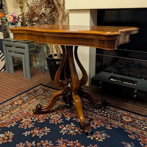 May include: A brown wooden table with a rectangular top featuring curved edges. The table is supported by a central pedestal base that branches into four ornate, curved legs with carved details at the feet, providing a stable foundation.