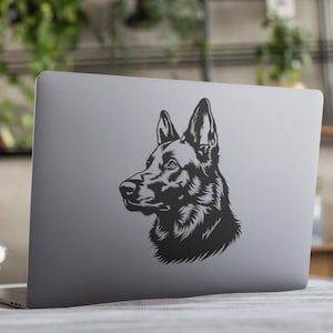 Może przedstawiać: Czarno-biała sylwetka głowy owczarka niemieckiego wydrukowana na srebrnym laptopie.