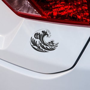 Puede incluir: Calcomanía de vinilo negro de una ola oceánica estilizada, aplicada a una superficie blanca de un coche. El diseño de la ola presenta una ola grande y rizada con detalles intrincados y una ola más pequeña en el fondo.
