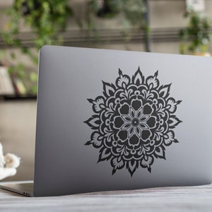 May include: A silver laptop with a black mandala sticker on the back. The mandala is intricate and detailed, with a floral design.
