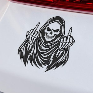 Puede incluir: Una pegatina de vinilo negro aplicada sobre la superficie blanca de un coche. El diseño gráfico muestra una figura de la parca esquelética con una túnica con capucha, con ambas manos esqueléticas levantadas haciendo una peineta.