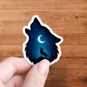 May include: A die-cut sticker depicting a wolf howling at the moon. The design shows a silhouette of a wolf on a hill, with a crescent moon and stars in a dark blue night sky. The sticker has a white border.