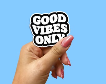 May include: A white sticker with black lettering that reads "GOOD VIBES ONLY" held in a hand with pink nail polish.