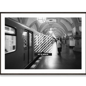 Könnte beinhalten: Schwarzweißfoto eines U-Bahnhofs in Berlin, Deutschland. Ein Zug fährt in den Bahnhof ein. Der Text "DIT IS BERLIN." ist auf dem Bahnsteig zu sehen.