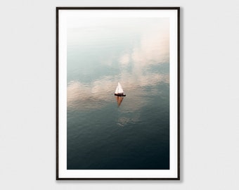 May include: A white sailboat with a brown hull sails on a calm body of water. The water is a deep blue colour and reflects the sky above. The sky is a light blue colour with white clouds.