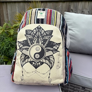 May include: A multi-coloured backpack with a cream front panel displaying a black Yin Yang symbol within a floral design. The backpack has striped patterns in red, yellow, and blue. The label reads "Himalaya Hemp".