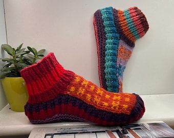 May include: A pair of handmade, knitted slipper socks. The socks feature a vibrant mix of colors, including red, orange, purple, and teal. The design includes textured patterns and a ribbed cuff. These cozy socks are perfect for indoor wear.