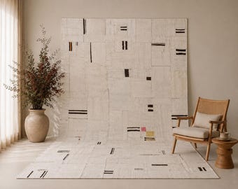 May include: A large, off-white area rug featuring a patchwork design of rectangular segments. The rug is decorated with scattered, thin black horizontal and vertical lines, along with small, singular pink and yellow square accents.