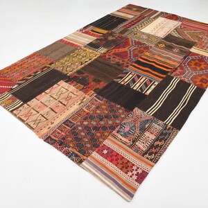 May include: A rectangular area rug composed of various stitched fabric patches featuring diverse geometric patterns and a multi-colored palette including shades of red, brown, black, orange, cream, and blue in a patchwork design.