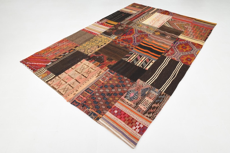 May include: A rectangular area rug composed of various stitched fabric patches featuring diverse geometric patterns and a multi-colored palette including shades of red, brown, black, orange, cream, and blue in a patchwork design.