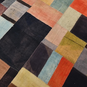 Può includere: Un tappeto patchwork con un design geometrico. Il tappeto presenta una varietà di colori, tra cui nero, rosso, arancione, blu e marrone. Il tappeto è composto da pezzi rettangolari di tessuto cuciti insieme.