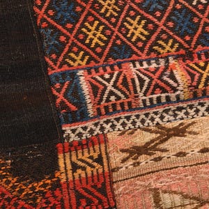 May include: A textile piece featuring a patchwork design with woven sections. One section displays a dark blue, red, and yellow diamond pattern. Another area shows a light beige and pink section with brown geometric embroidery and stitched details.