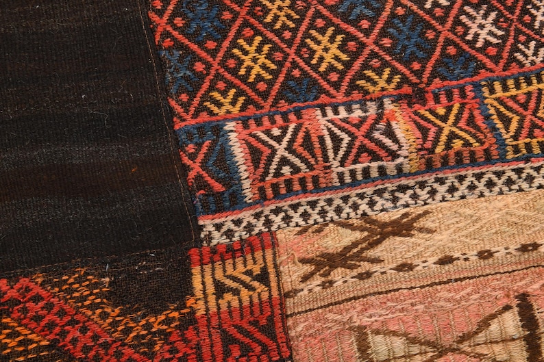 May include: A textile piece featuring a patchwork design with woven sections. One section displays a dark blue, red, and yellow diamond pattern. Another area shows a light beige and pink section with brown geometric embroidery and stitched details.