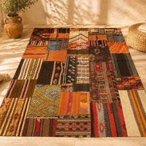 Puede incluir: Una alfombra rectangular grande de patchwork con varios patrones geométricos en tonos marrón, naranja, negro y crema. La alfombra está colocada sobre un suelo de madera clara, con un otomán tejido y objetos decorativos.
