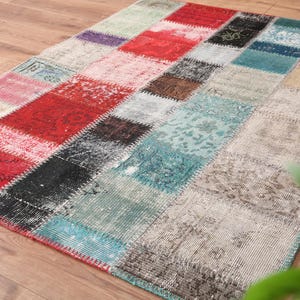 Puede incluir: Una alfombra rectangular de patchwork con una variedad de colores, incluyendo rojo, negro, turquesa y beige. La alfombra está hecha de múltiples piezas rectangulares cosidas juntas. La alfombra está colocada sobre un suelo de madera.