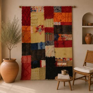 May include: A large rectangular wall hanging composed of various fabric patches in shades of red, yellow, orange, blue, and black. The textile features a mix of textures, including woven, fringed, and solid sections, suspended from a horizontal rod.