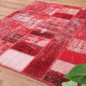 Peut inclure: Un tapis patchwork rouge rectangulaire avec diverses nuances de rouge et de blanc. Le tapis est composé de pièces rectangulaires de différentes textures et motifs, créant un aspect vintage. Le tapis est posé sur un sol en bois.