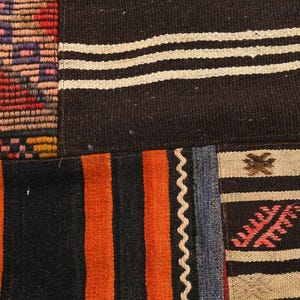 May include: A woven textile rug featuring a patchwork design of various patterns. Sections include black and white horizontal stripes, vibrant orange and black vertical stripes, and a multi-colored geometric grid with red, purple, and orange tones.