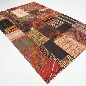 May include: A rectangular area rug composed of various stitched fabric patches featuring diverse geometric patterns and color palettes including deep red, black, brown, orange, yellow, and cream. The textile surface displays a mix of woven textures.