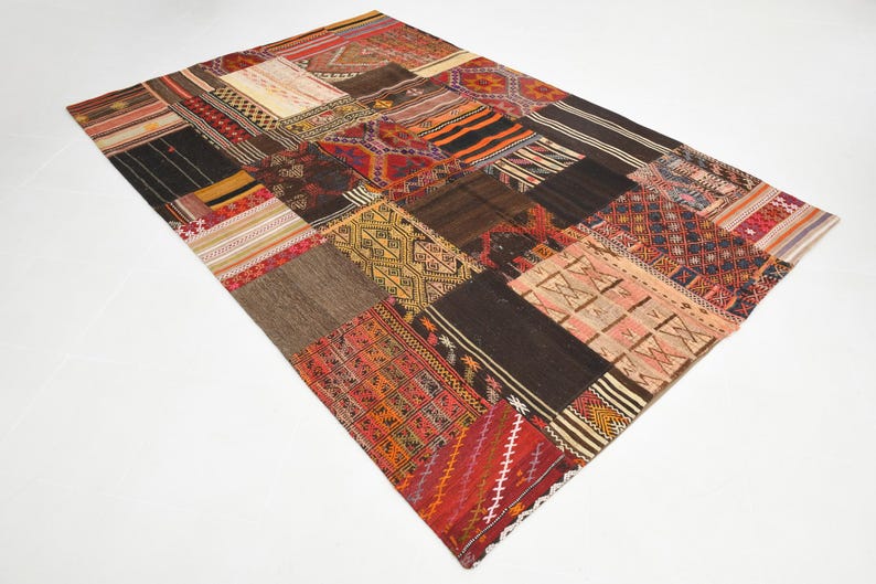 May include: A rectangular area rug composed of various stitched fabric patches featuring diverse geometric patterns and color palettes including deep red, black, brown, orange, yellow, and cream. The textile surface displays a mix of woven textures.