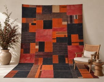 May include: A large area rug featuring a geometric patchwork design in shades of black, orange, red, and cream. The pattern consists of various rectangular and square blocks, some with solid colors and others with horizontal line textures.