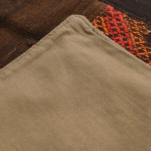 May include: A pillow cover featuring a solid light brown cotton fabric on one side and a dark brown woven textile with red and orange geometric patterns on the other. The cover has a visible seam along the edge where the two distinct fabrics meet.