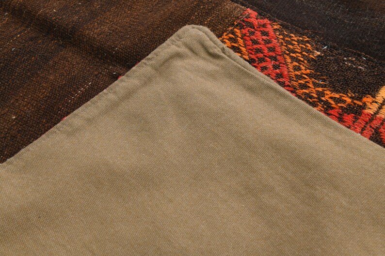 May include: A pillow cover featuring a solid light brown cotton fabric on one side and a dark brown woven textile with red and orange geometric patterns on the other. The cover has a visible seam along the edge where the two distinct fabrics meet.