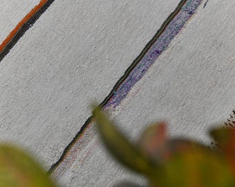 May include: Close-up of a textured, off-white rug with diagonal stripes in orange, black, and purple. The rug has a woven design and a fringed edge. The image is slightly out of focus.