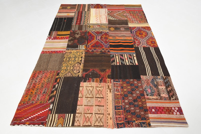 May include: A rectangular area rug composed of various stitched fabric patches featuring diverse geometric patterns and a multi-colored palette including shades of red, orange, yellow, brown, black, and cream in a woven textile construction.