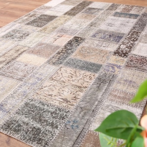 Puede incluir: Una alfombra rectangular de patchwork con una variedad de colores apagados, incluyendo beige, gris y marrón. La alfombra está hecha de numerosos parches rectangulares con diferentes patrones y texturas. La alfombra está colocada sobre un suelo de madera.