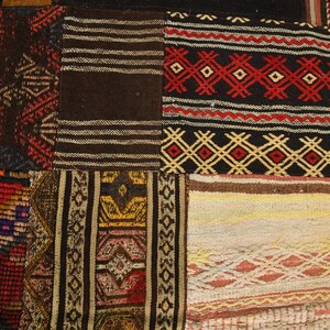 May include: A patchwork rug composed of various rectangular textile segments featuring woven geometric patterns in black, red, yellow, brown, and cream. The fabric sections display diverse linear, diamond, and zigzag motifs stitched together.