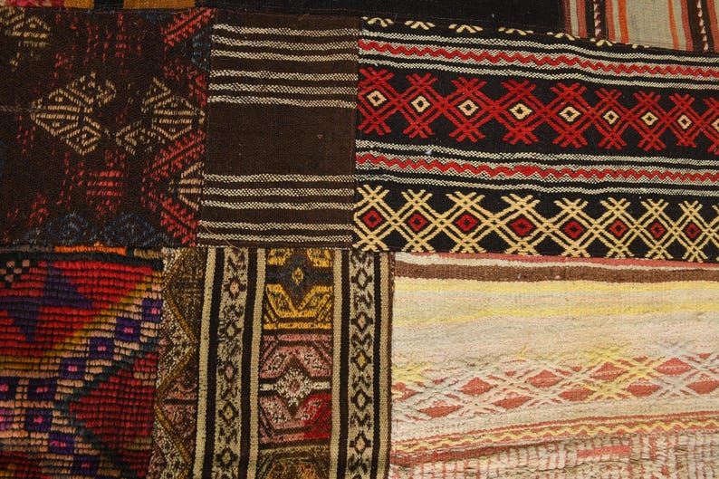 May include: A patchwork rug composed of various rectangular textile segments featuring woven geometric patterns in black, red, yellow, brown, and cream. The fabric sections display diverse linear, diamond, and zigzag motifs stitched together.