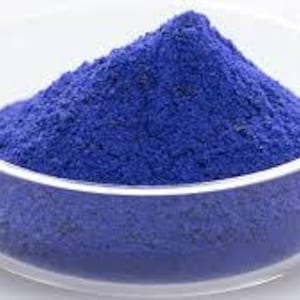 Puede incluir: Un cuenco de vidrio transparente lleno de un polvo azul vibrante. El polvo est&aacute; apilado en el centro del cuenco, creando una peque&ntilde;a monta&ntilde;a de color. El cuenco se encuentra sobre un fondo blanco liso.