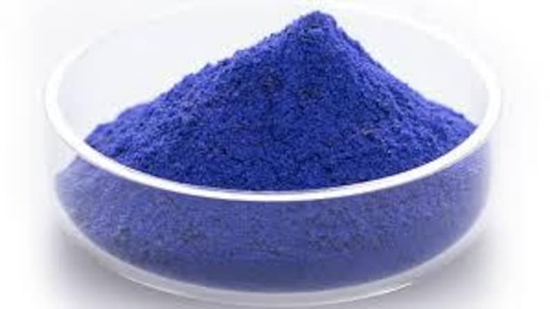 Puede incluir: Un cuenco de vidrio transparente lleno de un polvo azul vibrante. El polvo est&aacute; apilado en el centro del cuenco, creando una peque&ntilde;a monta&ntilde;a de color. El cuenco se encuentra sobre un fondo blanco liso.