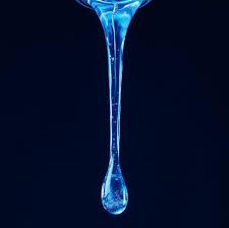 May include: A close-up of a single, elongated, blue liquid drop against a dark blue background. The drop is suspended mid-air, with a narrow stream flowing into a larger, tear-shaped droplet at the bottom. The liquid appears translucent, with subtle internal textures.