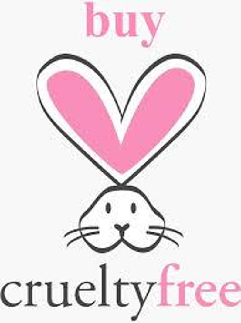 Puede incluir: Gr&aacute;fico de una cara de conejo blanco con bigotes negros y un contorno rosa en forma de coraz&oacute;n encima. Las palabras "buy" y "cruelty free" est&aacute;n en rosa y negro, colocadas encima y debajo del conejo.