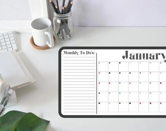May include: A rectangular dry-erase calendar for January, with a black border and a section for monthly to-do's. The calendar grid features colored dots and the word "January" in a stylish font. The calendar is on a white desk.