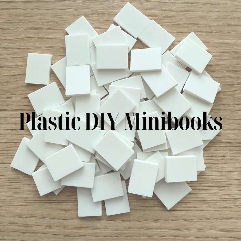 May include: A pile of small, white plastic rectangles on a light brown wooden surface. The text "Plastic DIY Minibooks" is displayed in black. These pieces are perfect for crafting miniature books and other DIY projects.