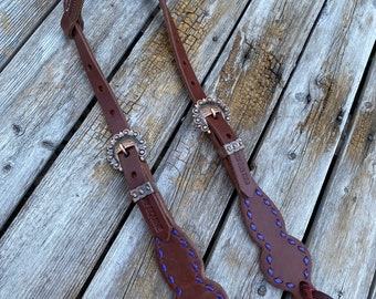 May include: A brown leather horse headstall with purple stitching and silver buckles. The headstall is decorated with a diamond pattern and the text "W.E.QUINE" is embossed on one side.