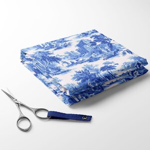 Puede incluir: Un trozo de tela blanca doblado con un patr&oacute;n de toile azul que presenta un dise&ntilde;o repetitivo de &aacute;rboles, edificios y figuras. La tela est&aacute; doblada en tres partes y tiene un ribete azul y blanco.