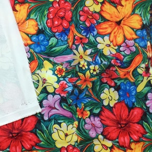 Op de afbeelding: Een kleurrijke bloemenstof met een verscheidenheid aan bloemen in tinten rood, geel, blauw en groen. De stof heeft een witte achtergrond en is perfect voor knutselprojecten.