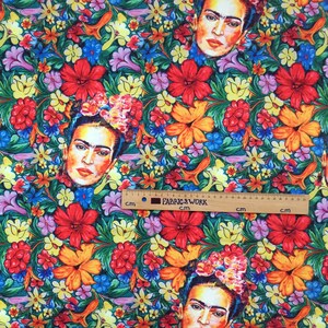 Op de afbeelding: Een kleurrijke stof met een herhalend patroon van bloemen en het gezicht van Frida Kahlo. De bloemen zijn in tinten rood, geel, oranje, roze, blauw en groen. De stof is perfect voor knutselprojecten, quilten en decoratie in huis.