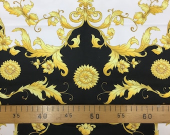 May include: Black and white fabric with a gold baroque pattern. The fabric features a repeating design of stylized leaves, flowers, and scrolls. A ruler is placed on the fabric, showing measurements in inches.