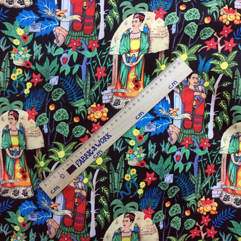 May include: Black fabric with a colorful repeating pattern of Frida Kahlo, parrots, flowers, and other tropical elements. The fabric is measured with a ruler in inches.